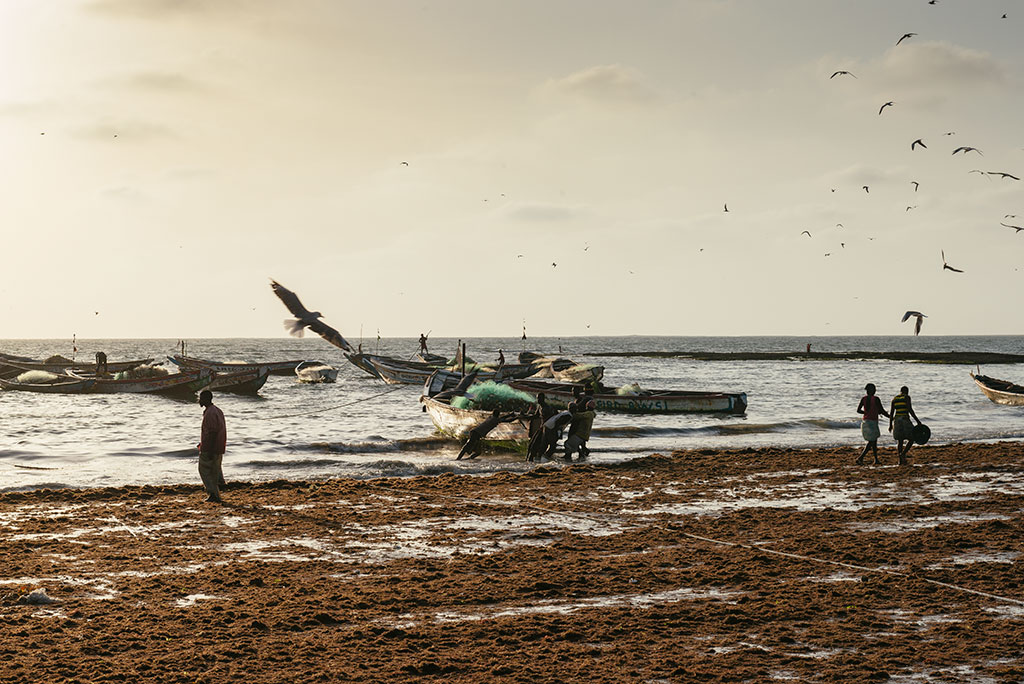 Hombres sacan su barca del mar en Tanji al atardecer